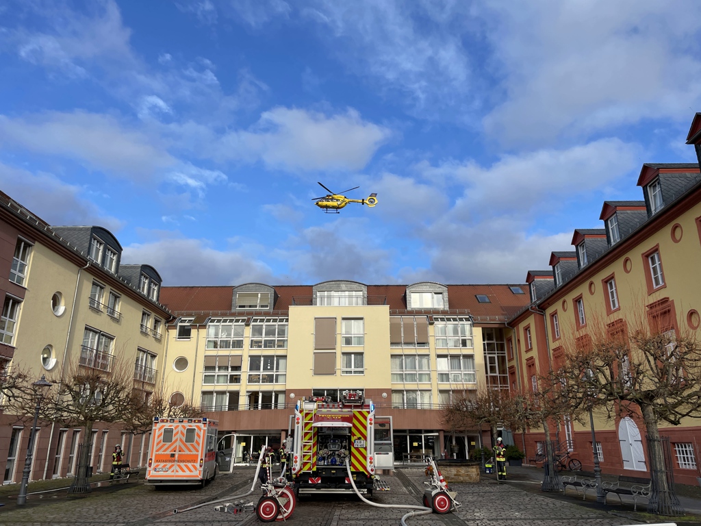 Rettungswagen, Löschfahrzeug stehen vor dem Seniorenheim, darüber schwebt ein Rettungshubschrauber